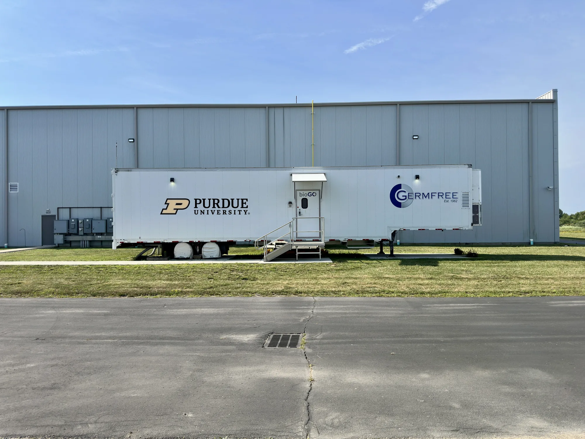 Purdue BioTrain mobile lab trailer from GermFree, mocked up with the Purdue University signature and the BioTrain molecule mark, parked beside a metal building.